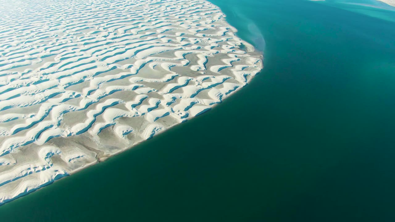 Opening aerial frame over Guerrero Negro, Baja California Sur, with rippled white sand dunes on the left and turquoise water on the right, no visible people.