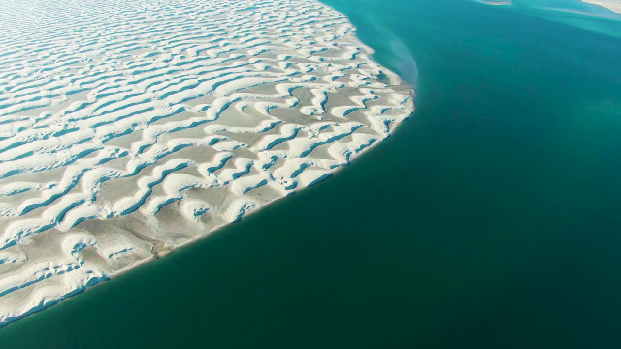 White dune patterns border a broad area of blue-green ocean.