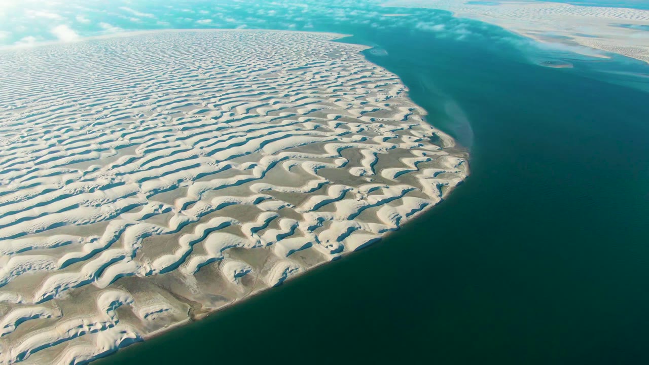 Opening aerial frame over Guerrero Negro, Baja California Sur, showing pale patterned dunes beside dark teal coastal water with no visible people.