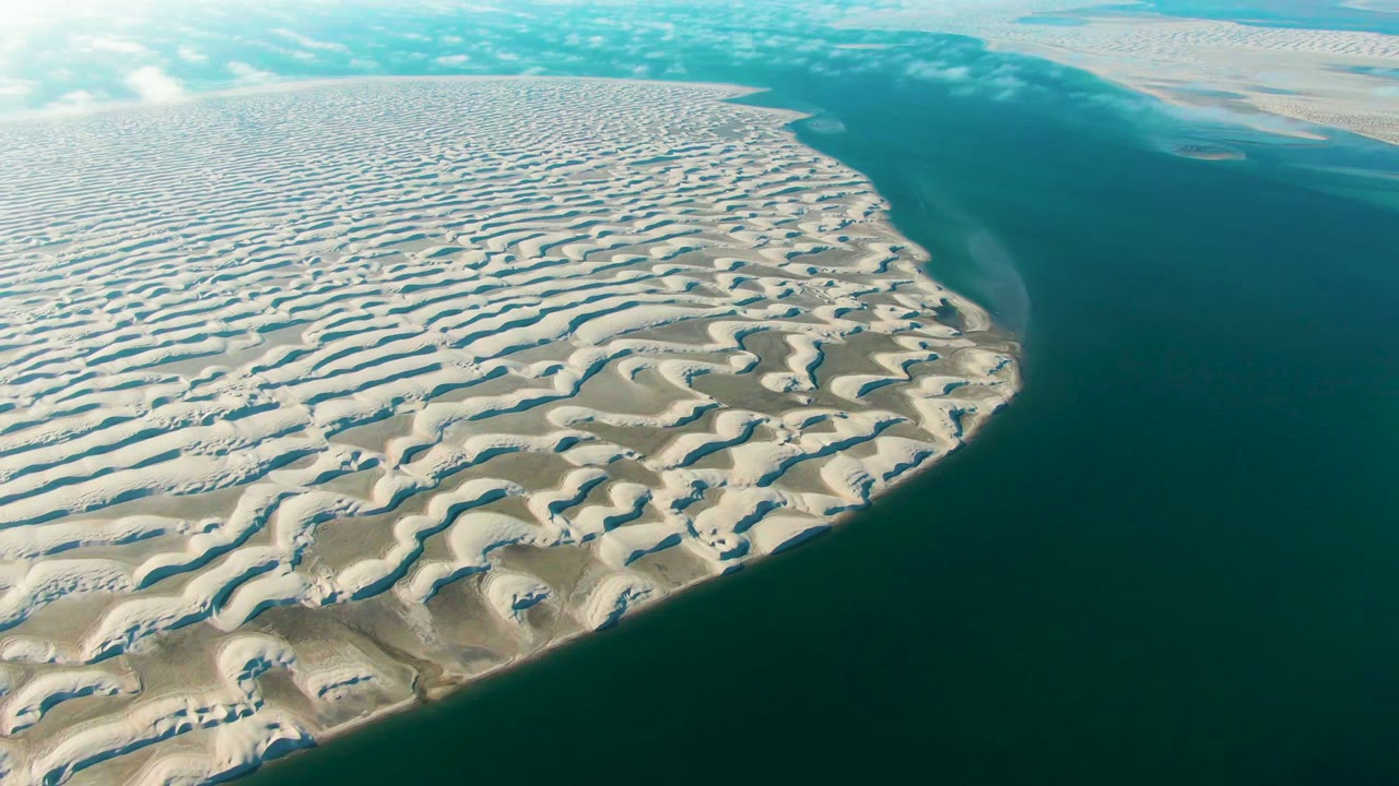 Patterned coastal dunes curve along a calm dark water channel.