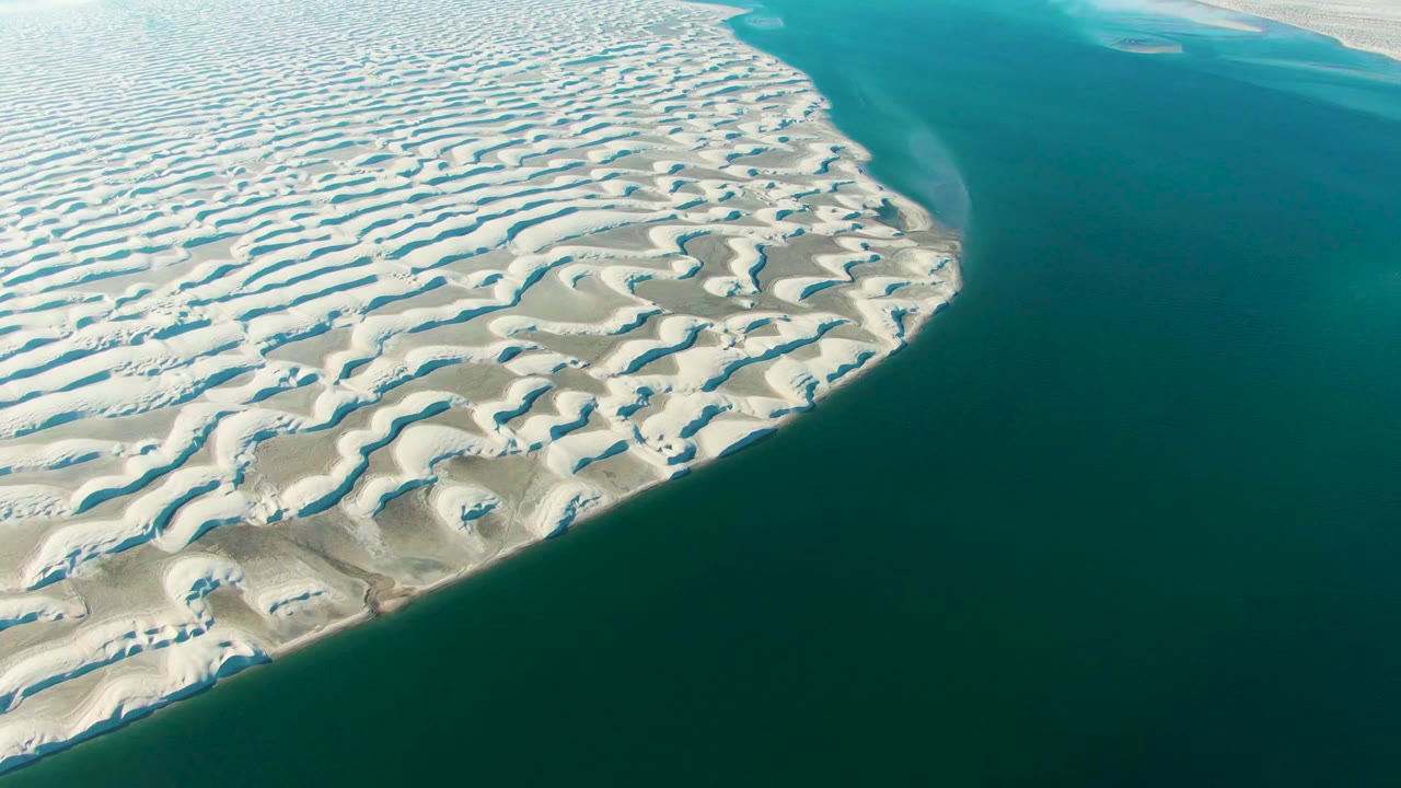 Patterned white dunes border dark turquoise water.