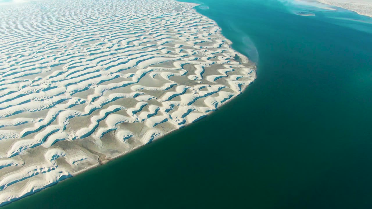 High aerial frame over Guerrero Negro where the pale dune shoreline arcs into blue-green lagoon water under soft cloud-filtered light, with no visible people.