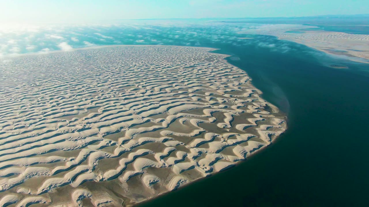 Wide aerial coastline with beige dune ridges and blue-green water.