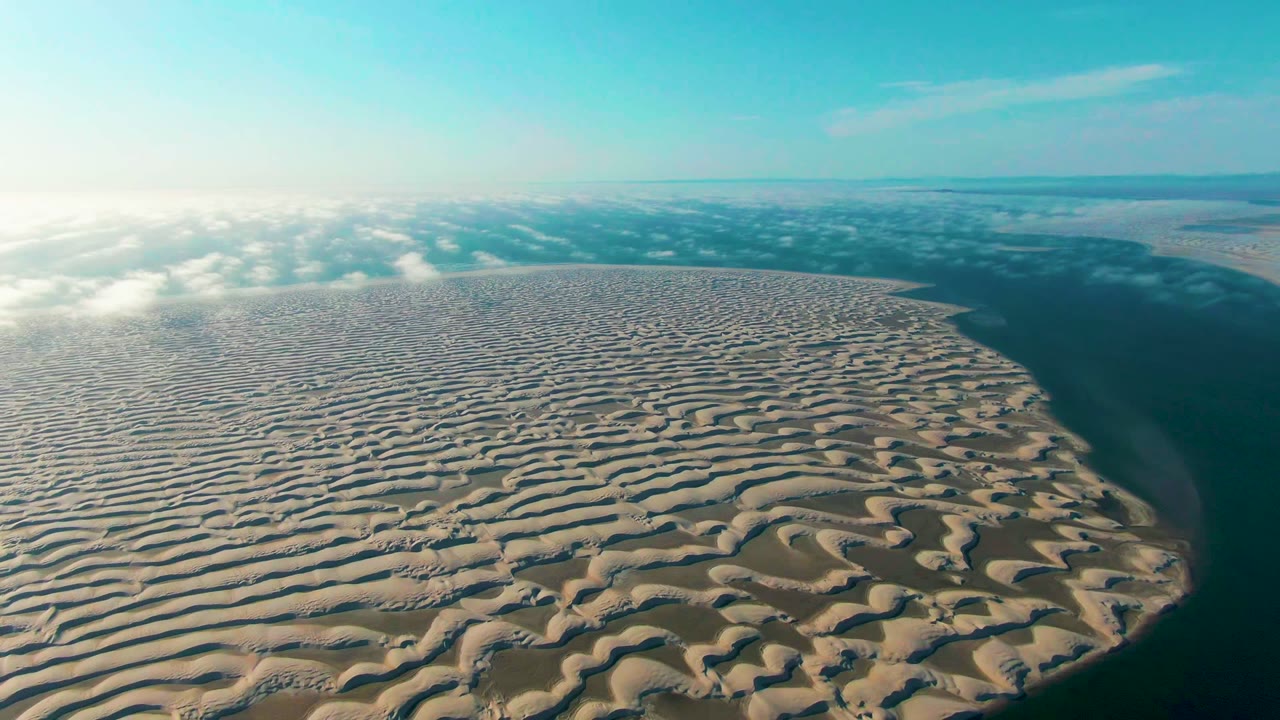 Rippled dune field curves toward dark water below a blue sky.