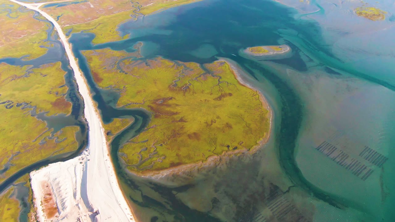 Aerial road and marsh channels beside shallow turquoise water