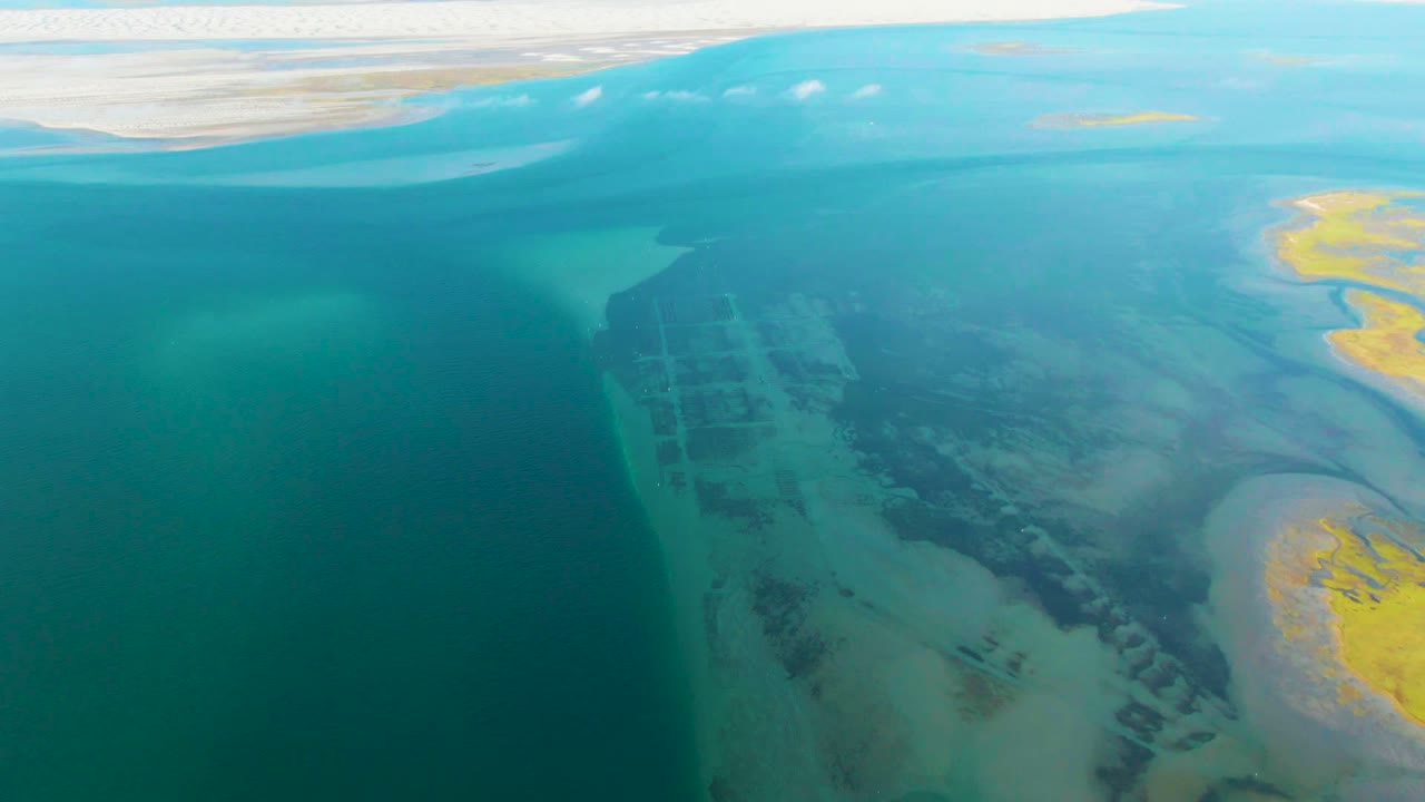 Overhead coastal water with pale sandbars and darker seabed patterns