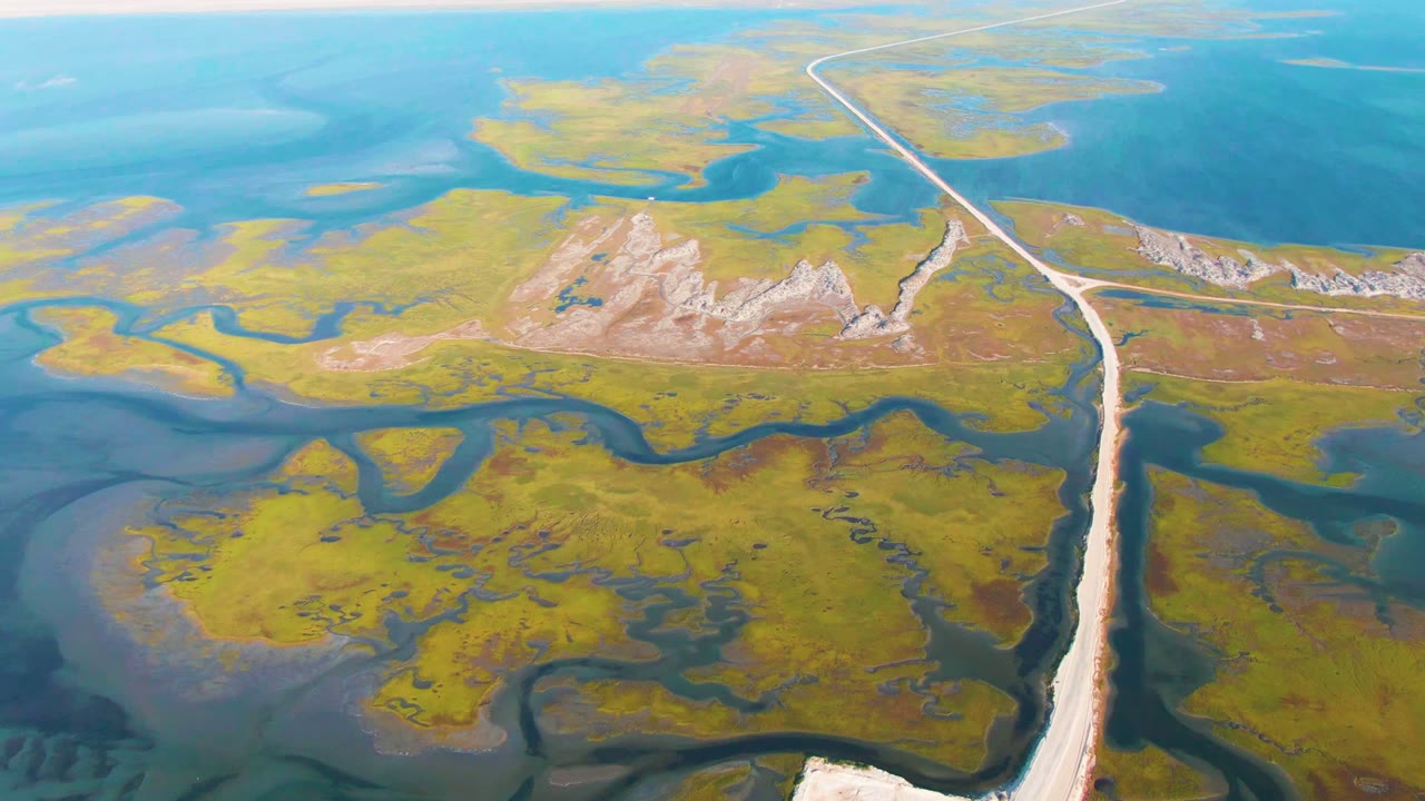 High aerial view of wetlands with a road running from foreground toward open water.
