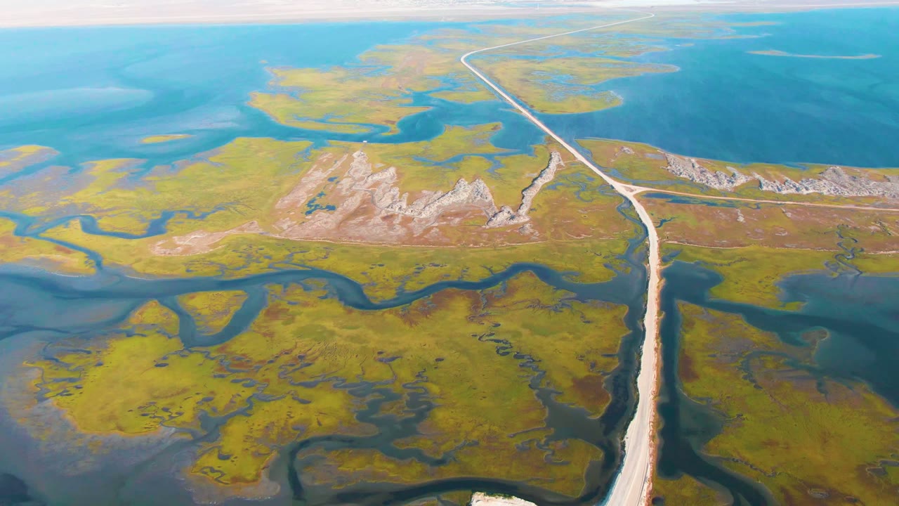 Road running from foreground toward distant water through marshland