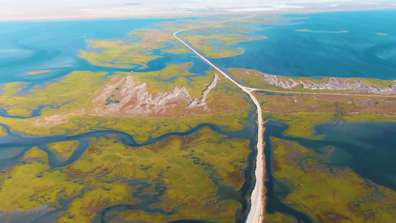 Drone view of a pale road dividing marsh channels and open blue water