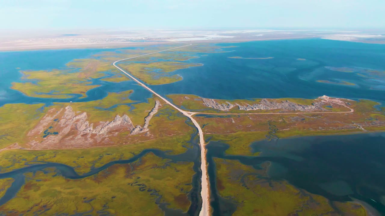 Aerial view of road, rocky mounds, wetlands, and broad blue lake water.