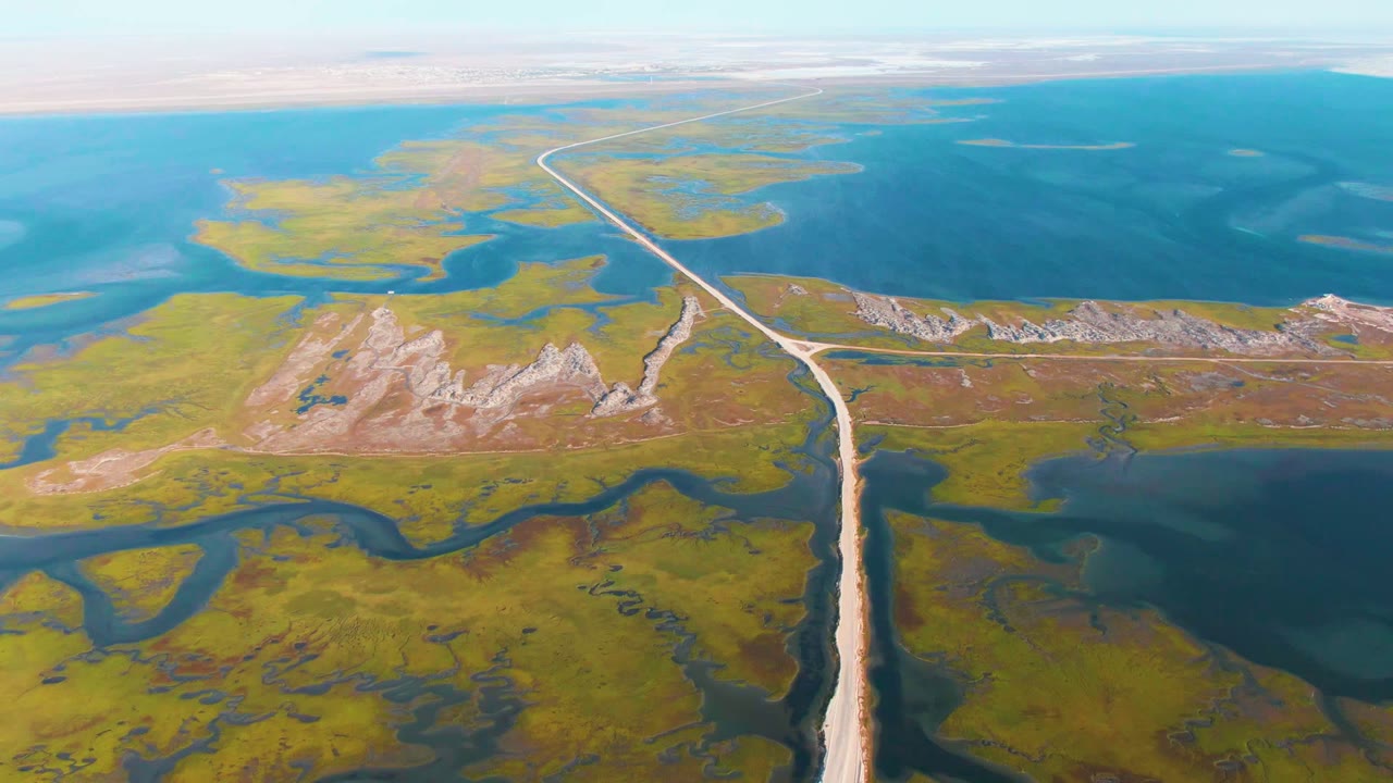 Drone view of a road dividing marshland and blue lagoon water.