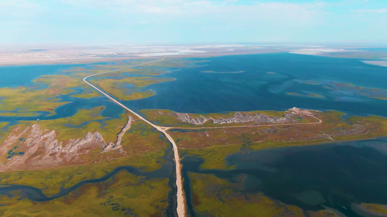 High aerial view of a dirt road leading toward open water.