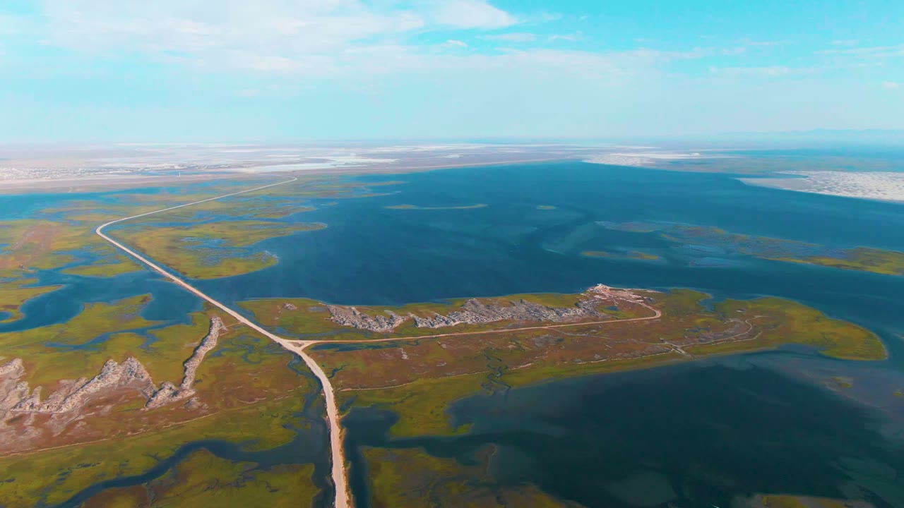 Aerial frame from Guerrero Negro, Baja California Sur with the dirt road leading from the lower frame toward marshy islands and a broad blue water body, with no visible people.