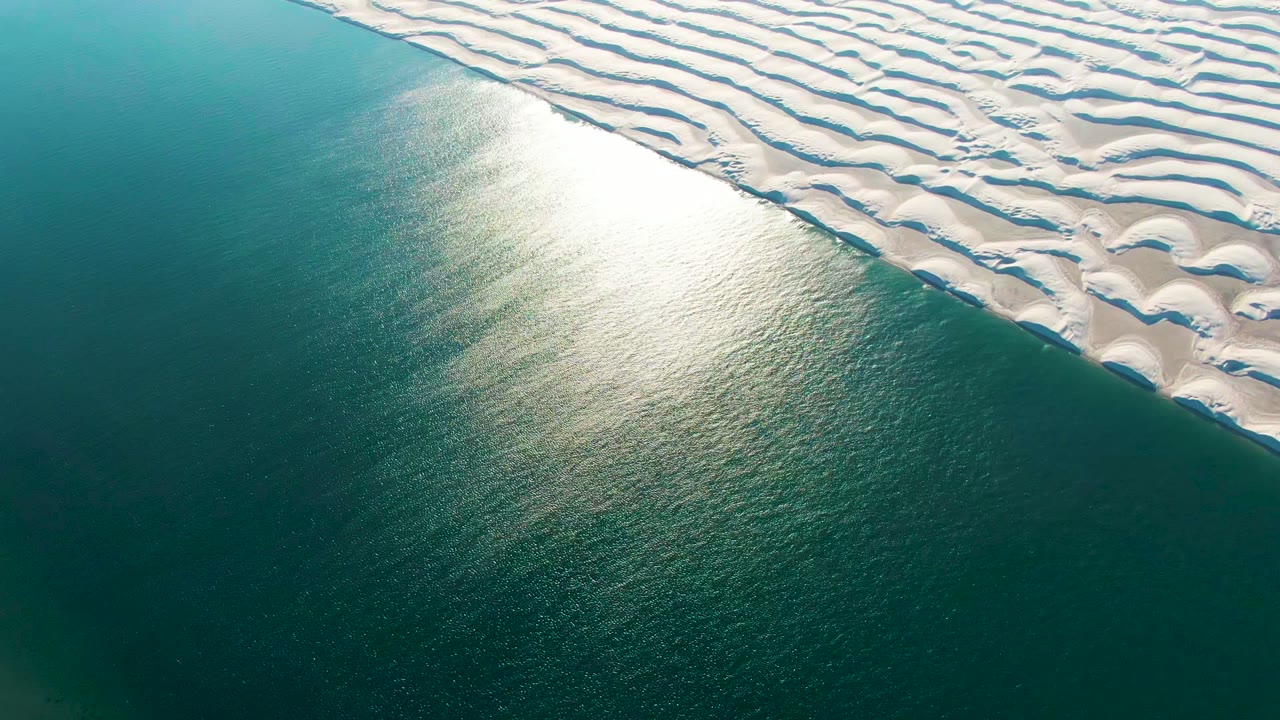 White dune edge bordering turquoise water under strong reflected light.