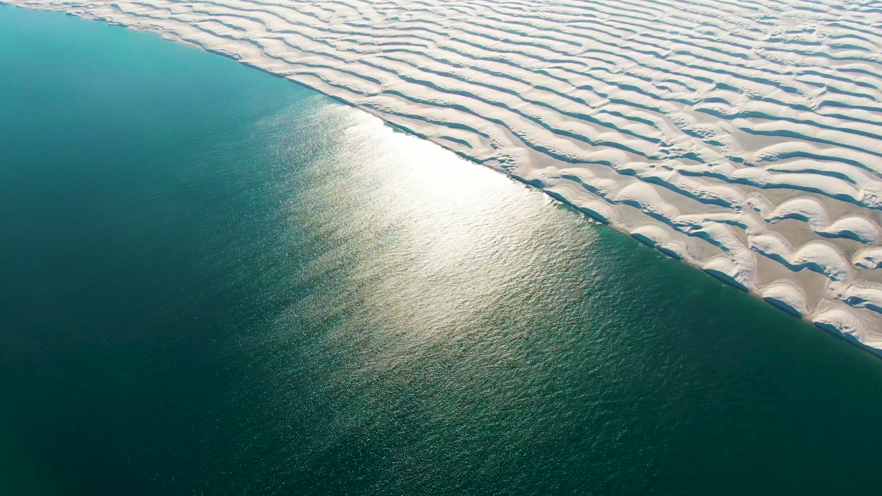 At 0:00, an aerial view in Guerrero Negro shows white rippled dunes meeting teal ocean water with a bright sun reflection and no visible people.