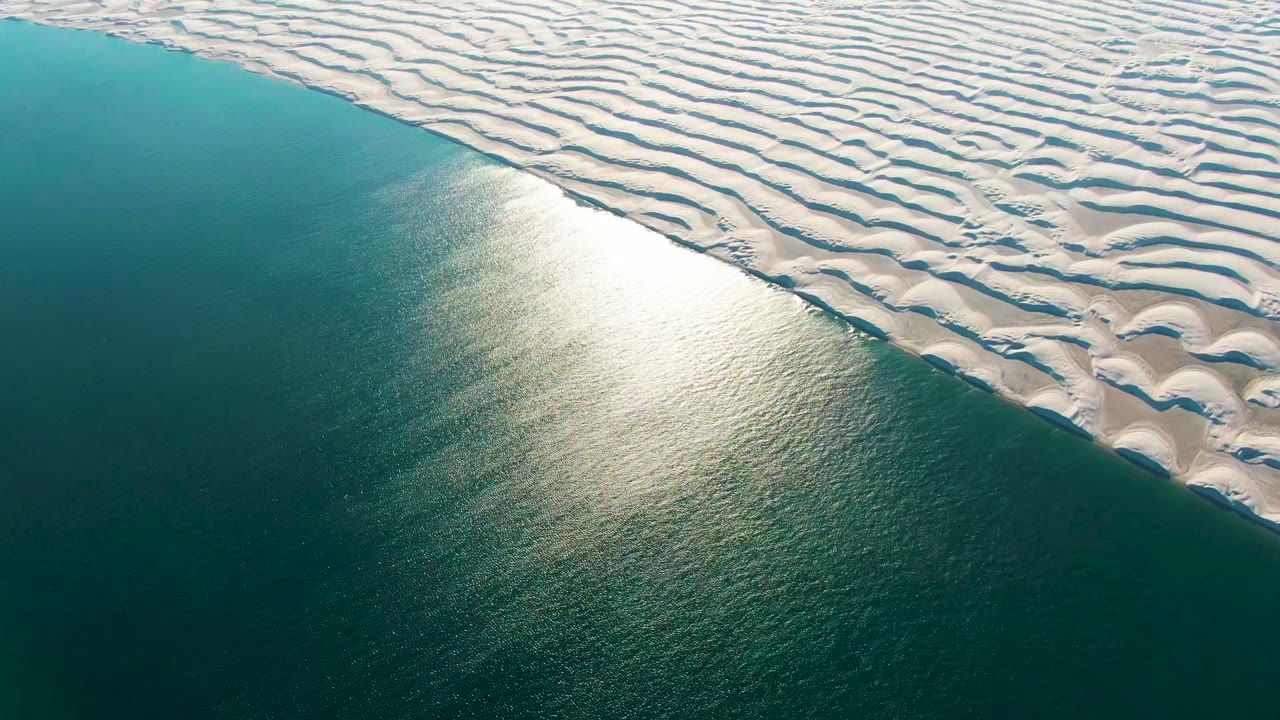 White dune ridges border calm teal water with sun glare
