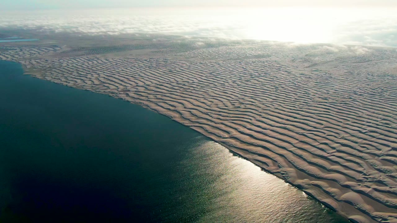 Coastline aerial with sunlit water and patterned sand