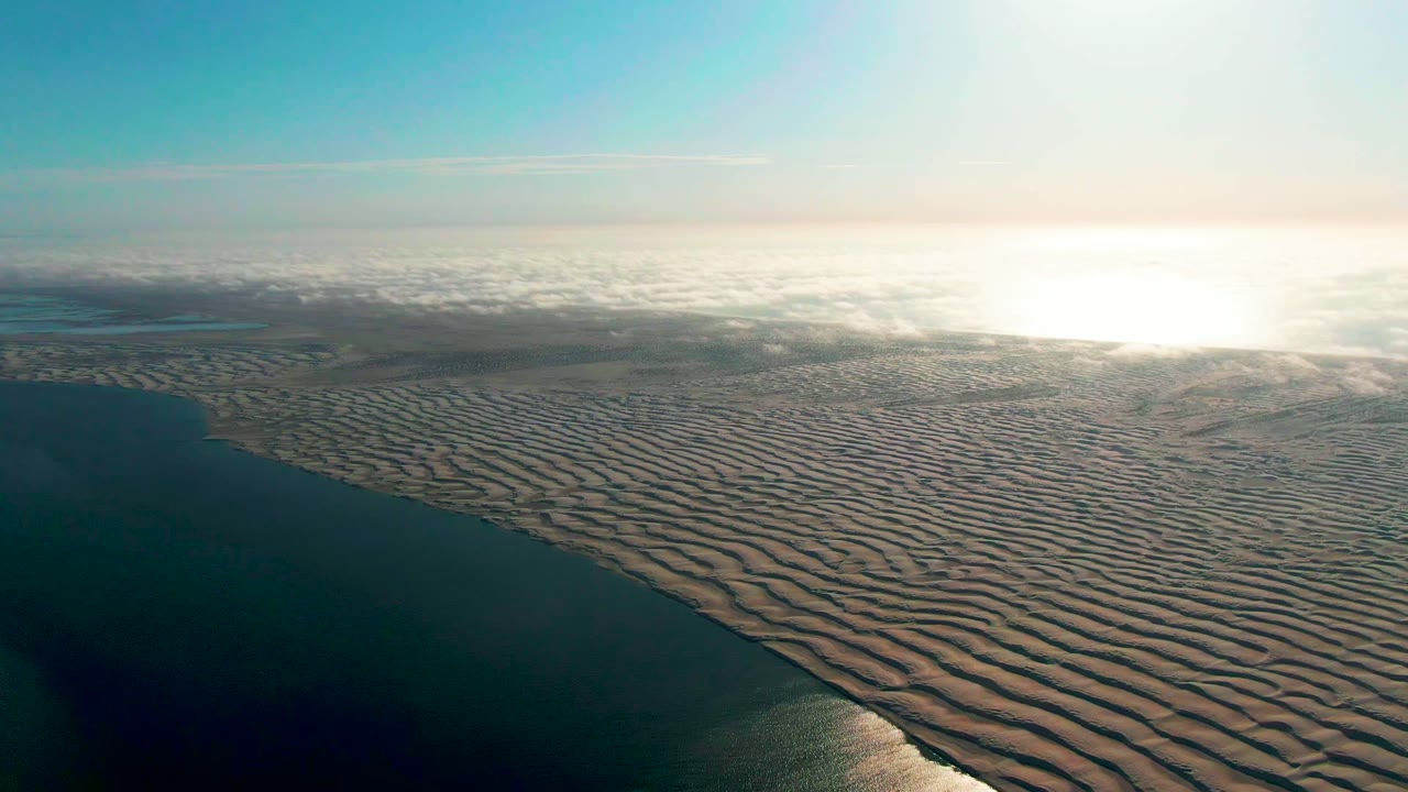 Rippled coastal sand and calm ocean seen from above.