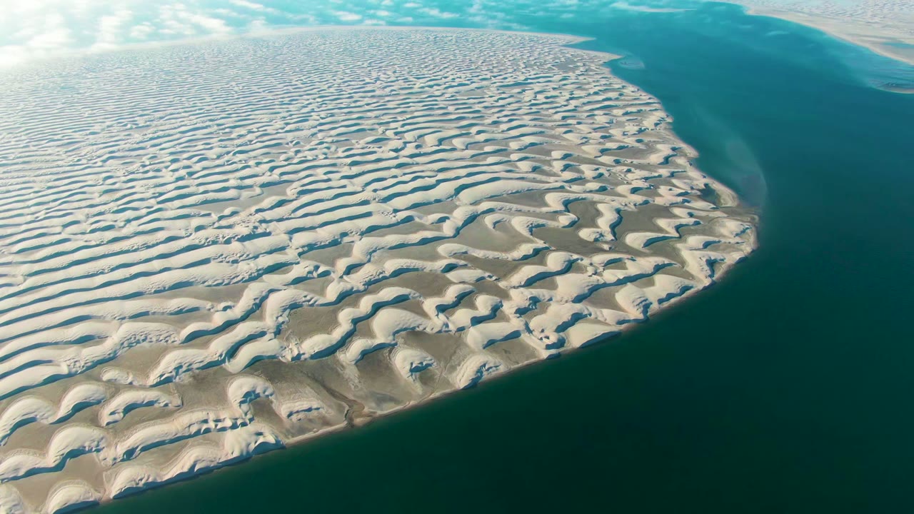 Aerial view over Guerrero Negro, Baja California Sur, with rippled pale sand dunes curving beside blue-green ocean and no visible people.