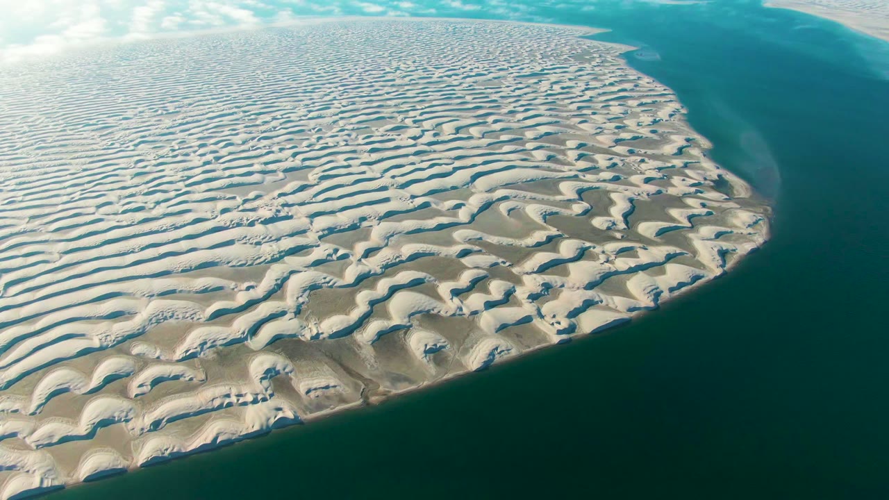 Aerial frame from Guerrero Negro, Baja California Sur showing rippled beige sand curving toward dark blue water at the right edge, with no visible people.