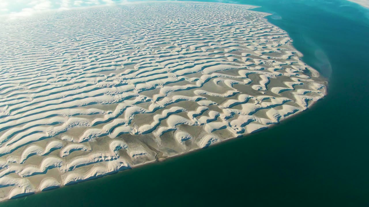 Aerial frame from Guerrero Negro, Baja California Sur showing the rounded end of a rippled sand formation bordered by calm blue water, with no visible people.