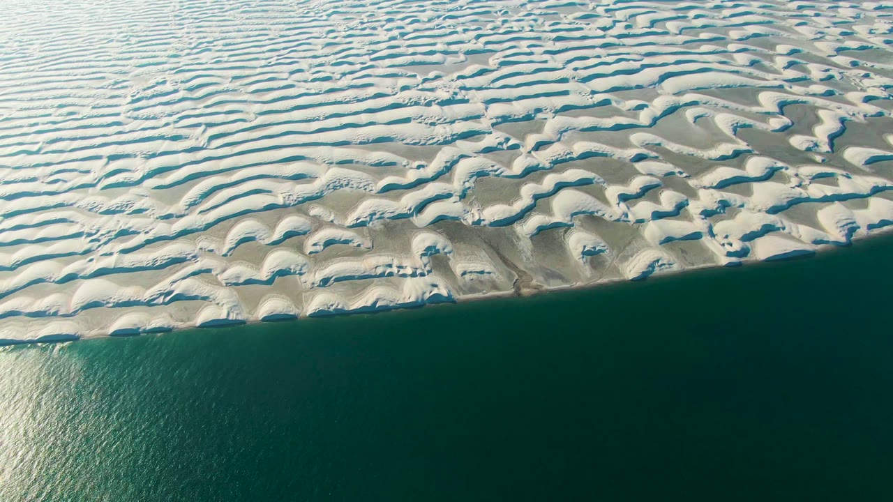 Aerial frame in Guerrero Negro, Baja California Sur, showing bright reflection on the left side of the water below pale dunes, with no visible people.