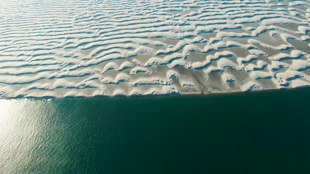 Bright water reflection beside patterned dunes and a straight shoreline.
