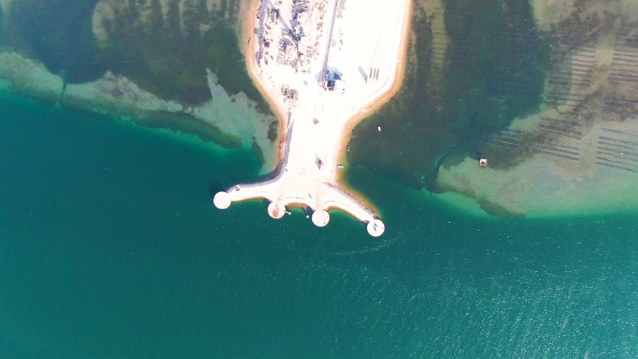 Aerial beach pier with people near the sand and clear water.