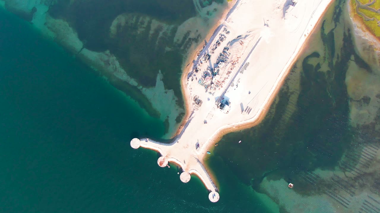 Aerial view of a white sandy peninsula and small boats near shore.