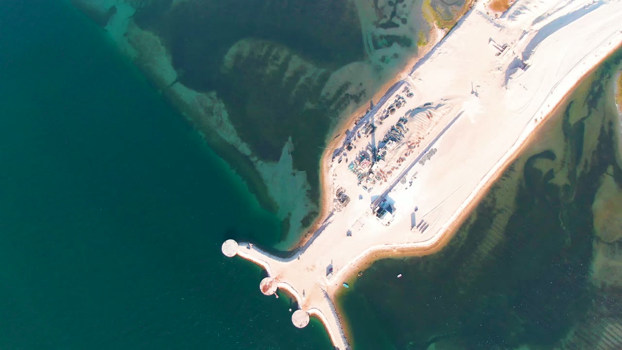 At 0:00, an overhead aerial frame shows a pale causeway and rounded road end in Guerrero Negro, Baja California Sur, with dark teal water to the left, green shallows around the edges, and no visible people.