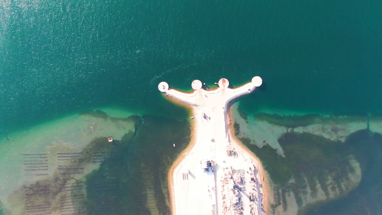 Overhead pier view with clear water and a small sandy shoreline area.