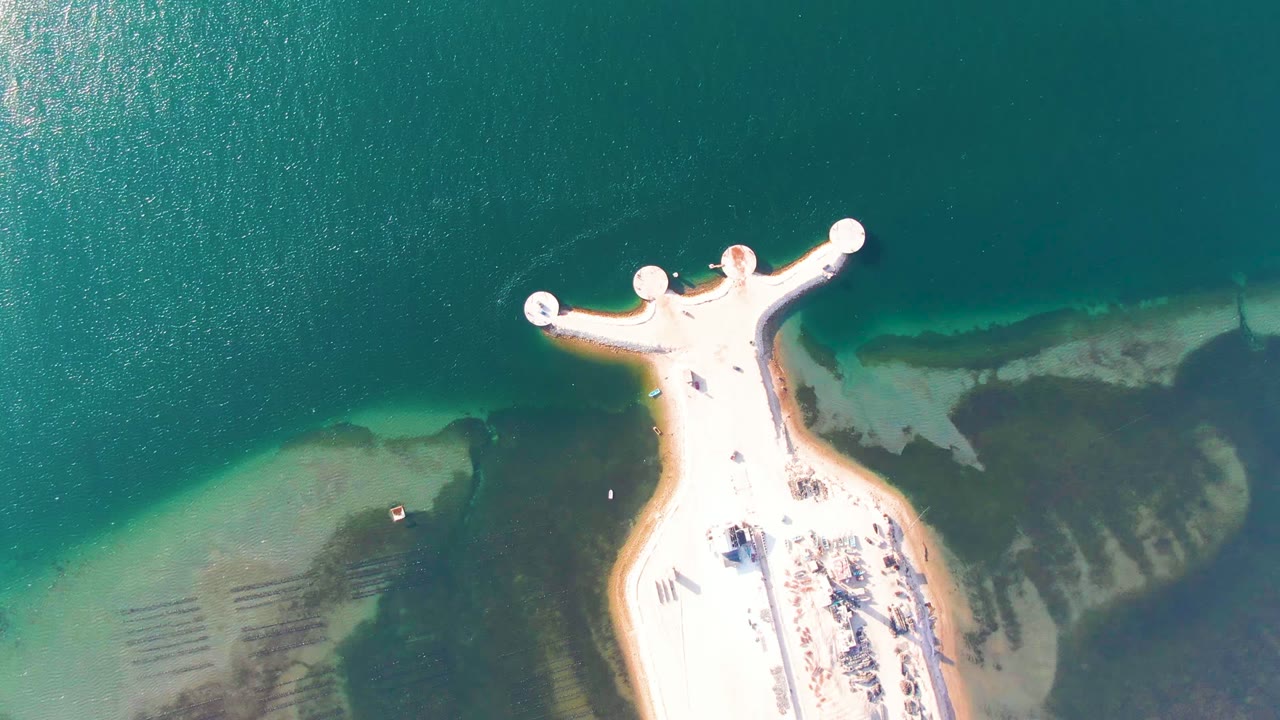Aerial view of a pale pier over blue-green water with a small boat near shore