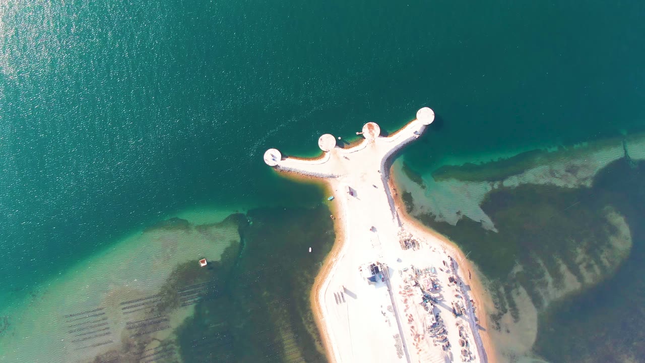 At 0:02, the high overhead view in Guerrero Negro emphasizes the rounded pier ends, bright pier surface, dark underwater patches, and no visible people.