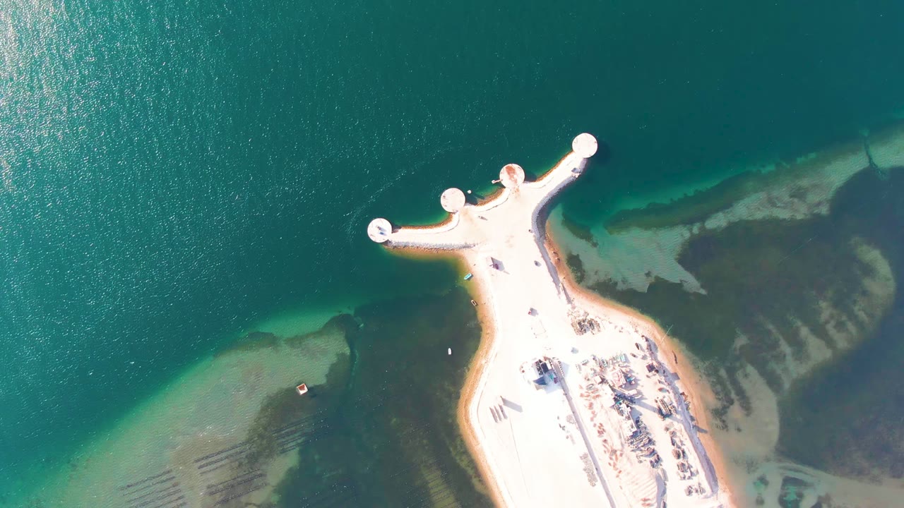 Overhead view in Guerrero Negro of a pale pier with circular dock ends extending into turquoise water, with sandy shallows and no visible people.
