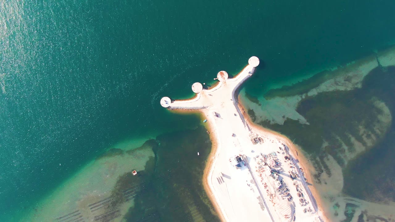 Aerial view of circular docks and clear water around a sandy point.