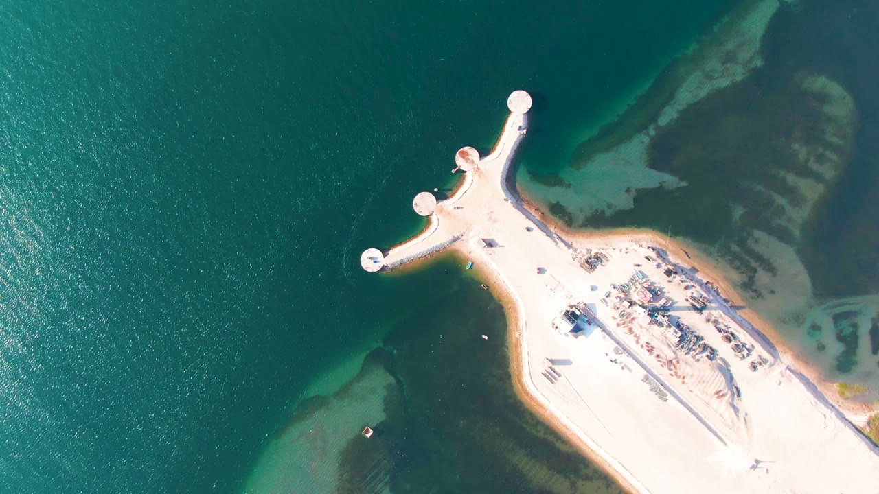 Top-down coastal pier with bright sand and darker shallow water.