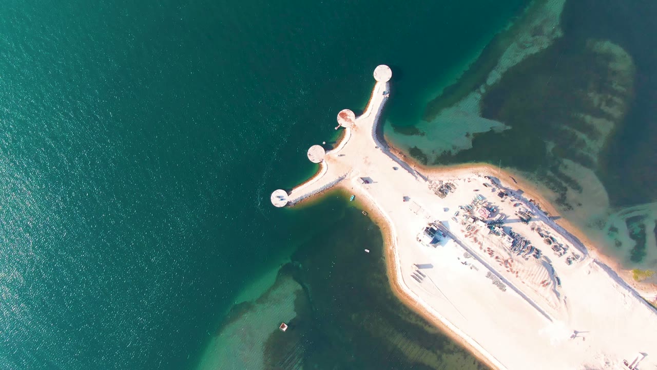 Aerial view over Guerrero Negro with the rounded pier ends visible, green ocean surface around them, pale sand at right, and no visible people.