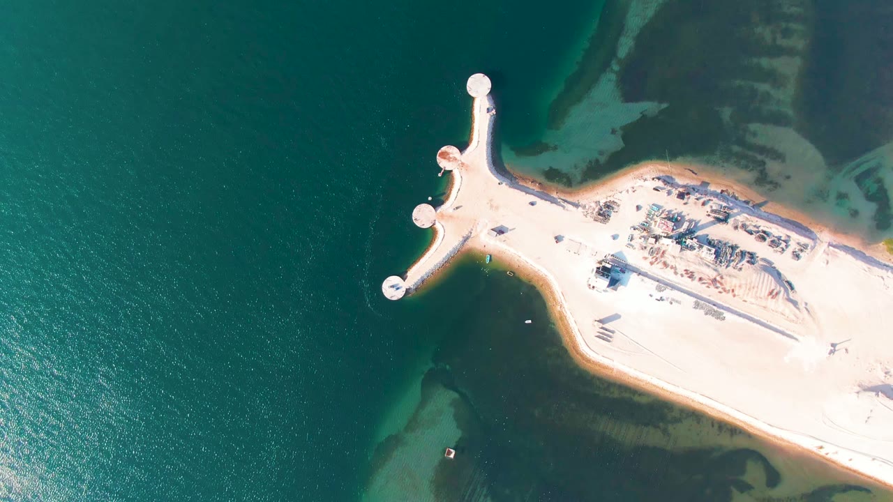 Aerial view of circular pier ends beside a bright sand shoreline.