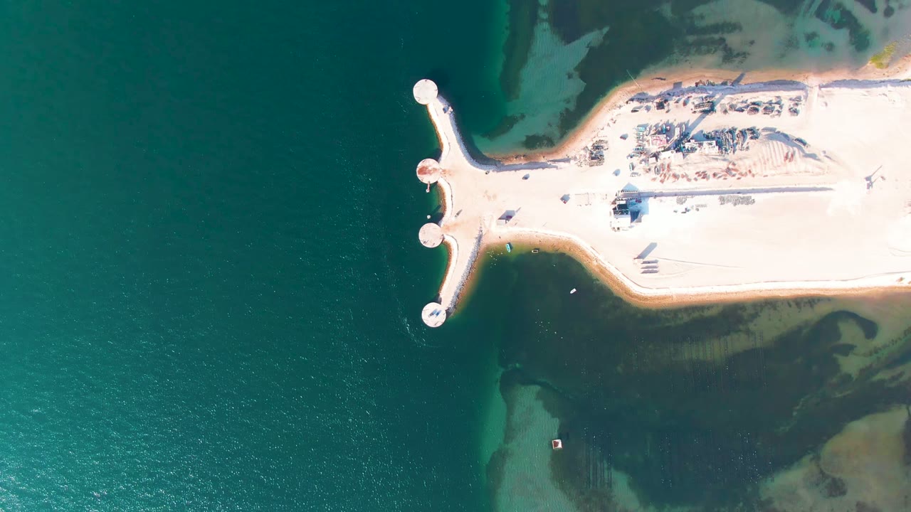 Overhead frame in Guerrero Negro, Baja California Sur showing a pale sandy pier with circular end markers reaching into teal water, with no visible people.