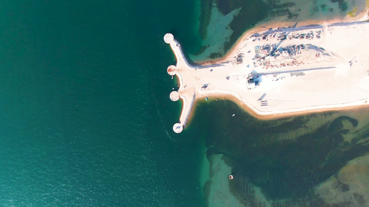 Sandy pier with circular markers surrounded by dark teal water.