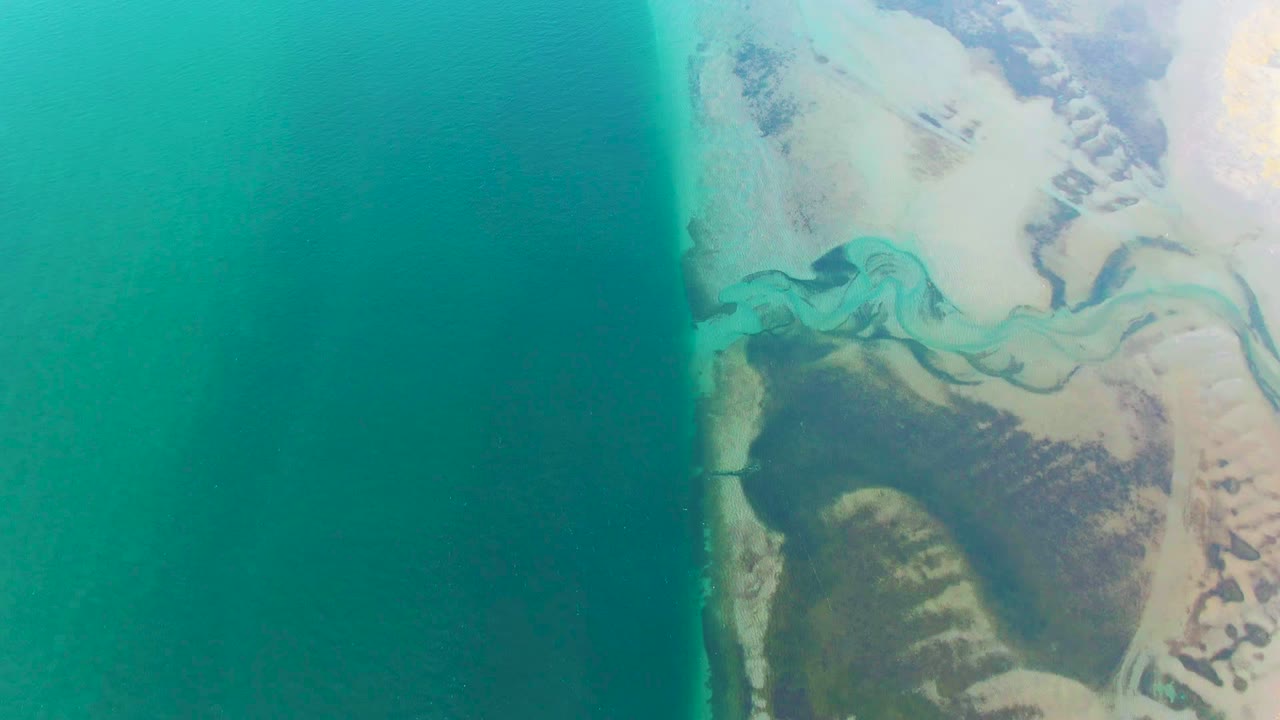 Overhead coastline with river channel entering turquoise water.
