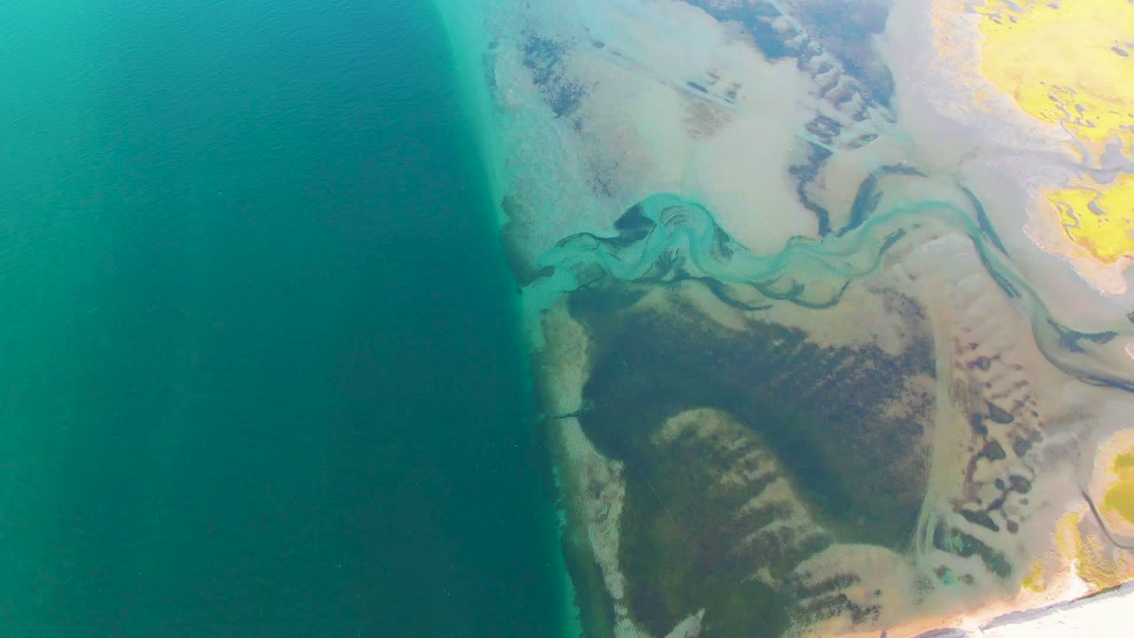 Teal ocean beside winding delta channels and darker shoreline vegetation.