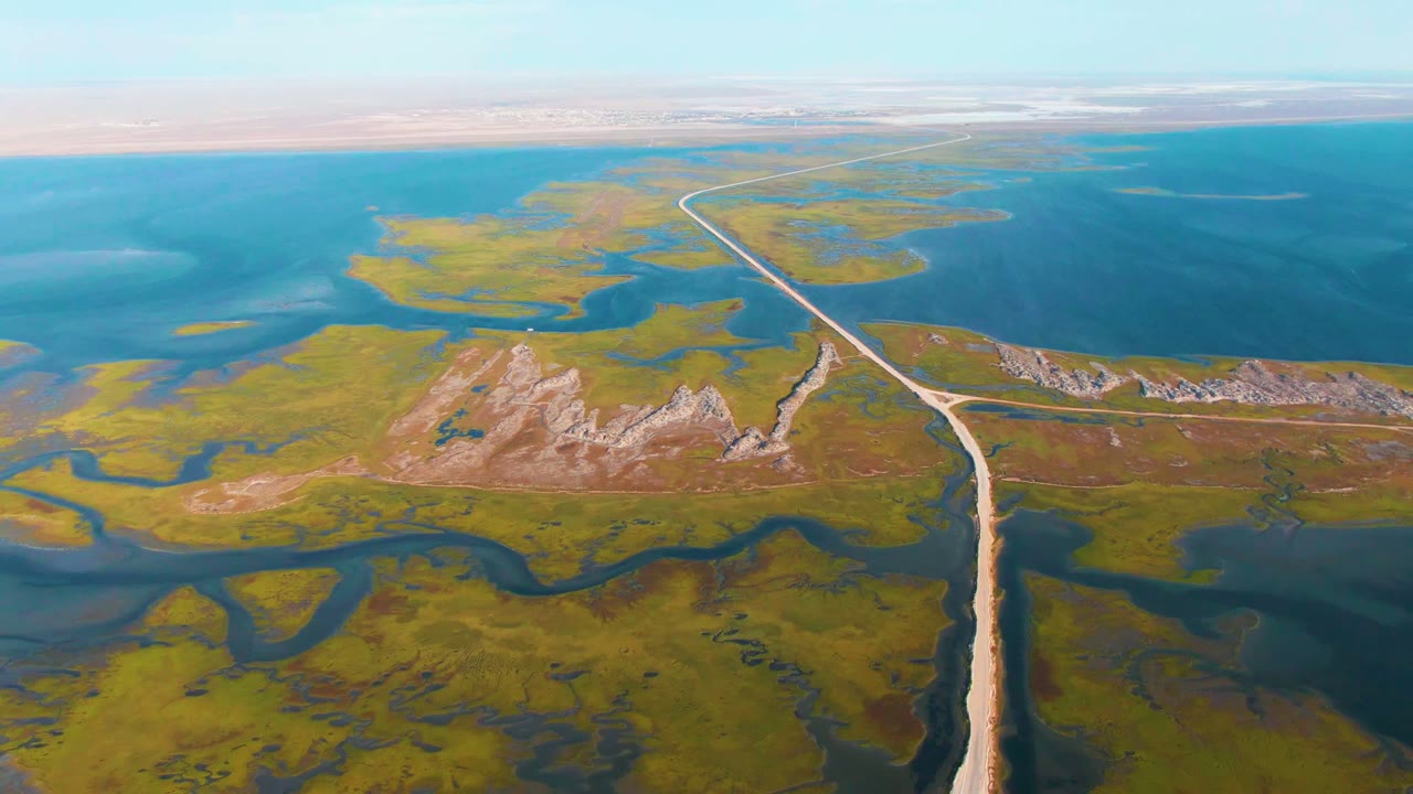 Drone view of a road bend beside rocky hills and marsh water.