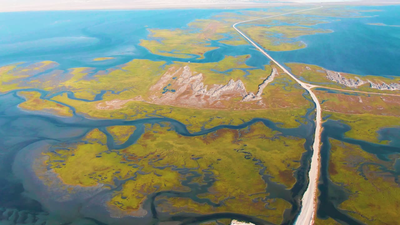 Aerial frame from Guerrero Negro, Baja California Sur showing a pale road running through green marsh islands and blue water channels, with no visible people.