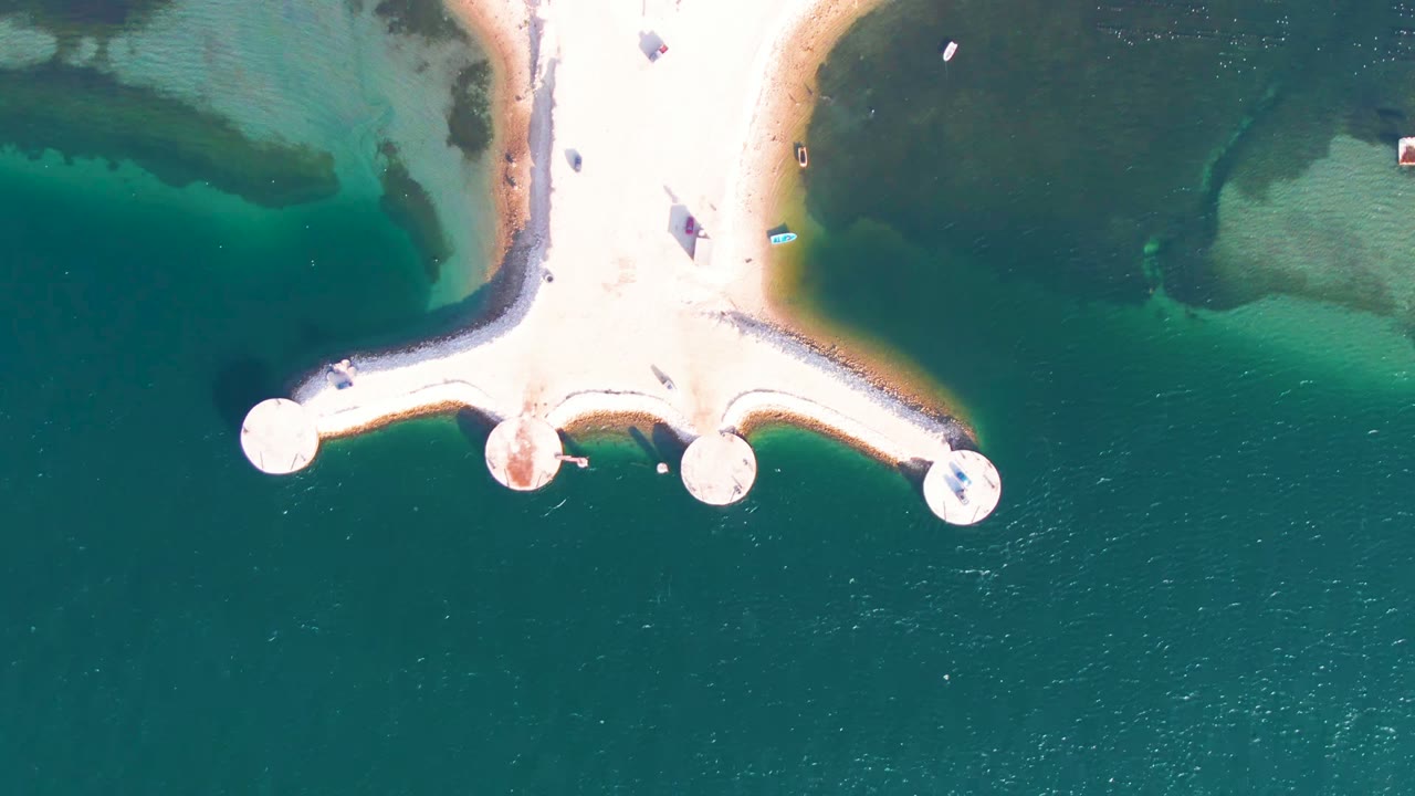 Overhead view in Guerrero Negro, Baja California Sur, showing a pale jetty with circular pier ends above turquoise and dark green shallow water, with no visible people.