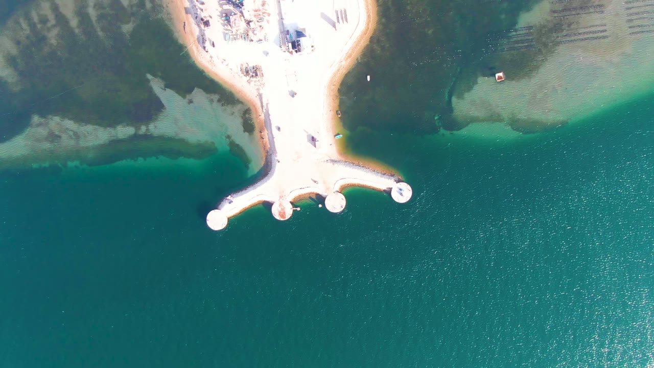 Aerial view of the dock and bright sandy shore beside darker shallows.
