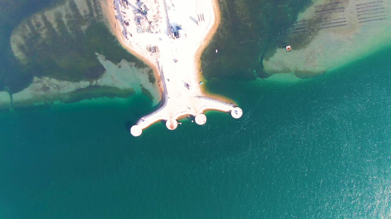 Straight-down frame in Guerrero Negro, Baja California Sur showing the dock projecting from the sandy beach into clear green-blue water, with no visible people.