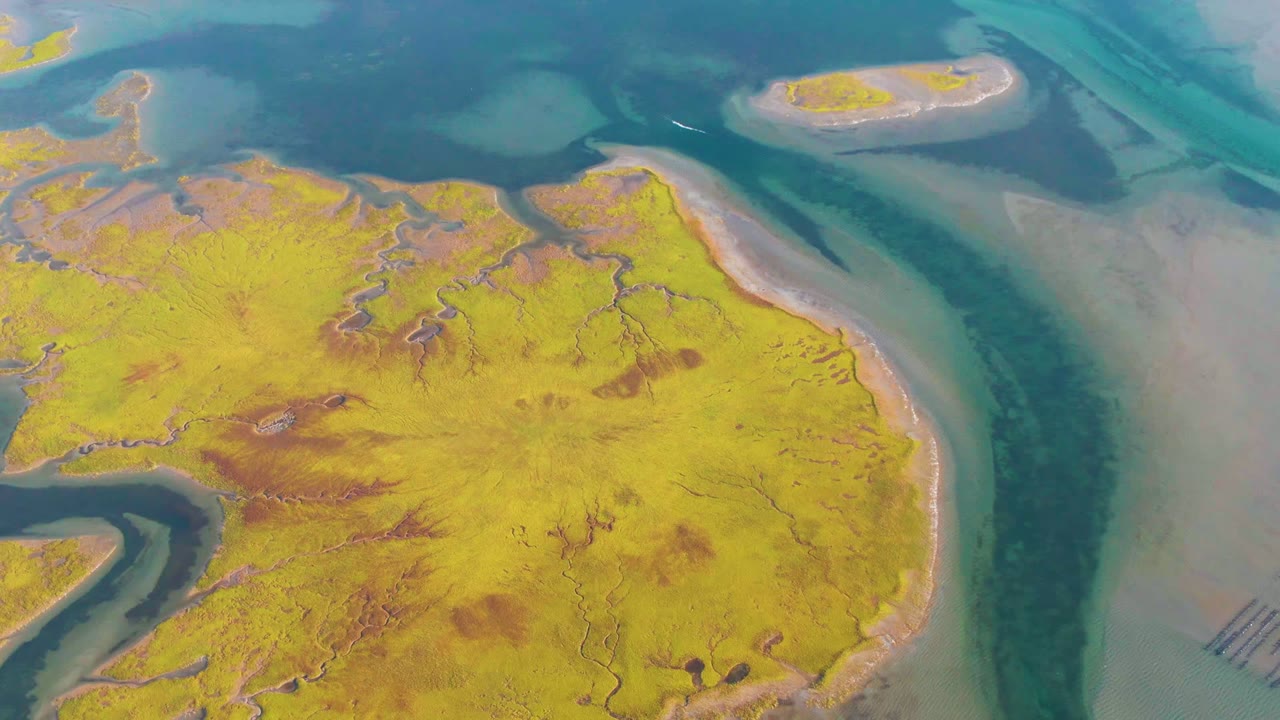 Opening aerial frame over a yellow-green sandbar and blue tidal channels in Guerrero Negro, Baja California Sur, with small exposed islands and no visible people.
