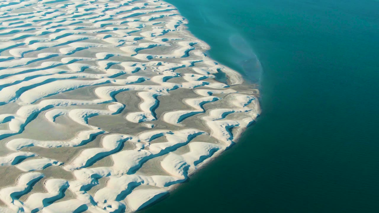 Patterned white dunes meeting calm blue-green water