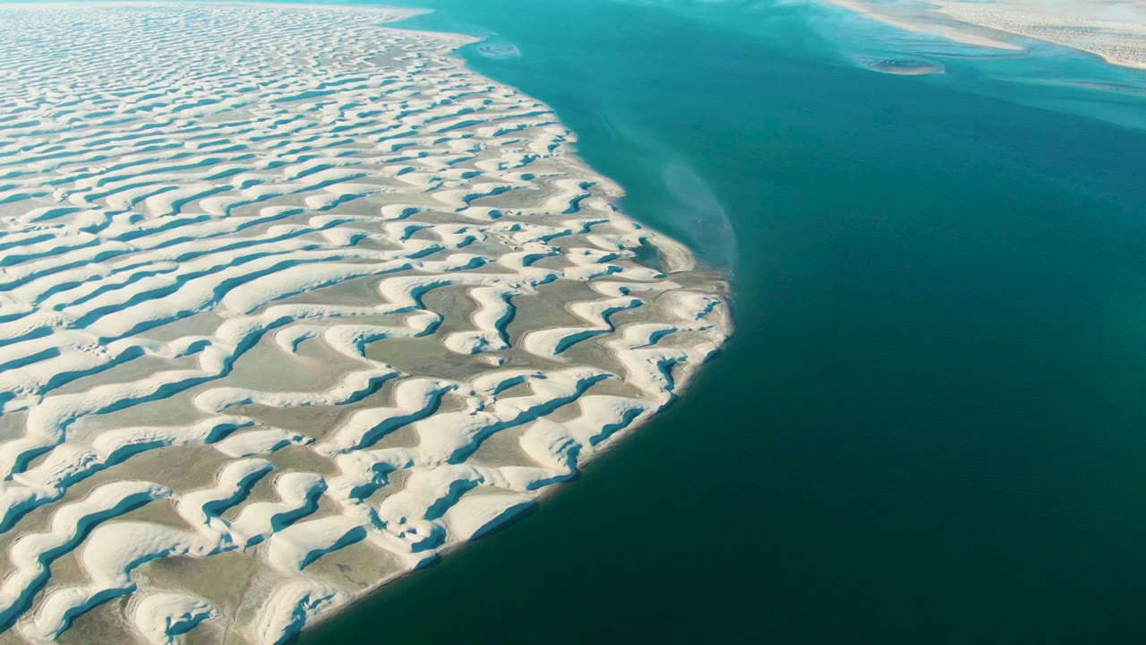 Aerial view of rippled white sand dunes meeting turquoise water in Guerrero Negro, Baja California Sur, with no visible people.